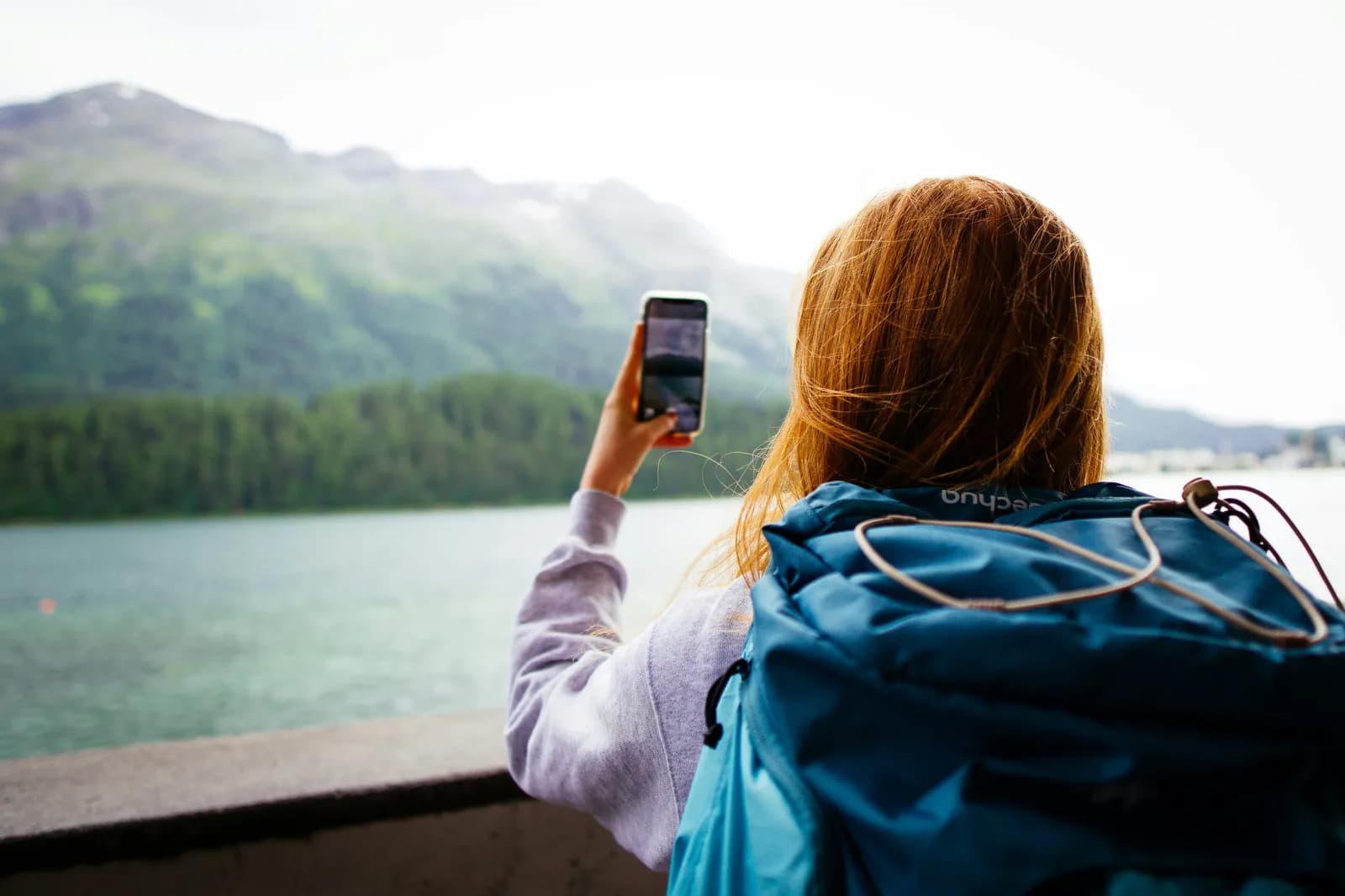 Traveler taking a photo with her phone at a mountain lake abroad